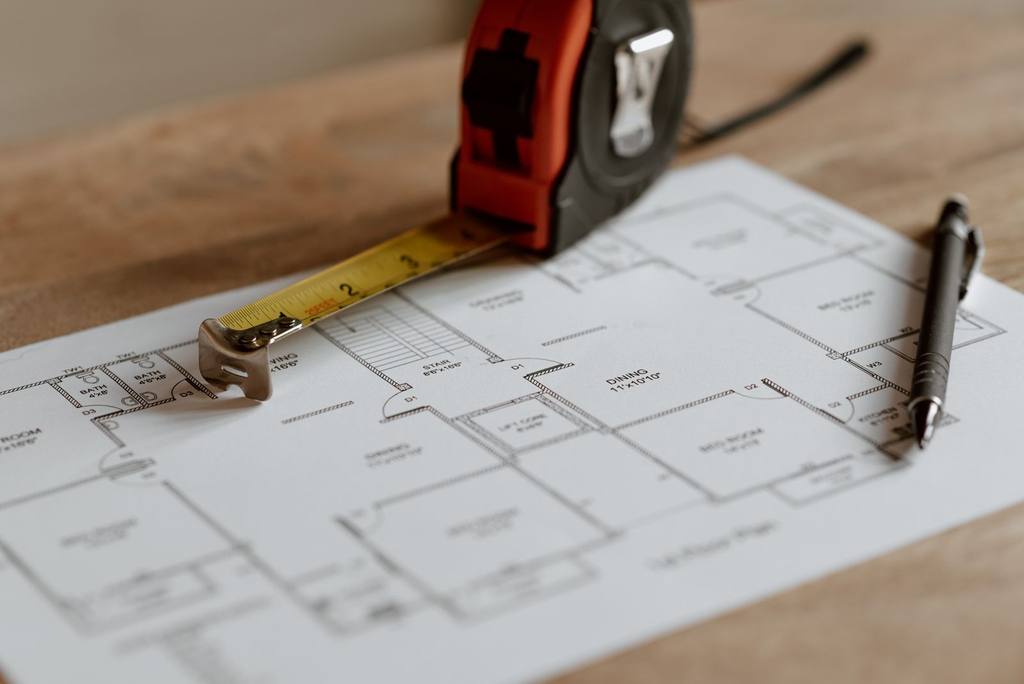 Architectural blueprint with a measuring tape and pen laid on a wooden table